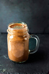 Organic natural chocolate coffee cacao smoothie beverage with chia seeds in glass jar with chocolate bar on a black graphite slate background, top view. Healthy diet vegetarian snack