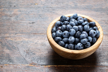 Freshly picked blueberries in wooden bowl on wooden background.
