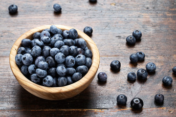 Freshly picked blueberries in wooden bowl on wooden background.