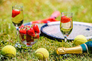 Tennis game. Strawberries, champagne and tennis balls with rackets on the green grass. Sport, recreation concept