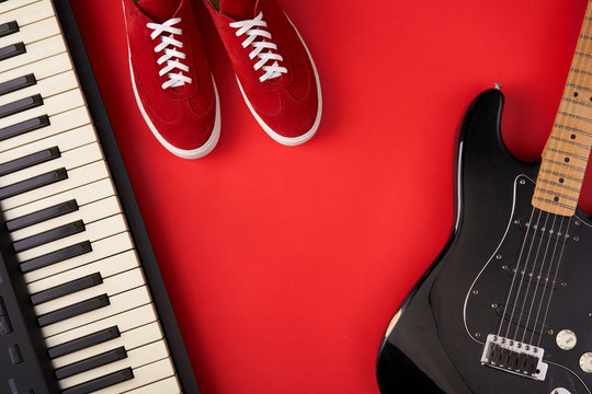 Electric guitar, synthesiser and red stylish sneakers, on red background