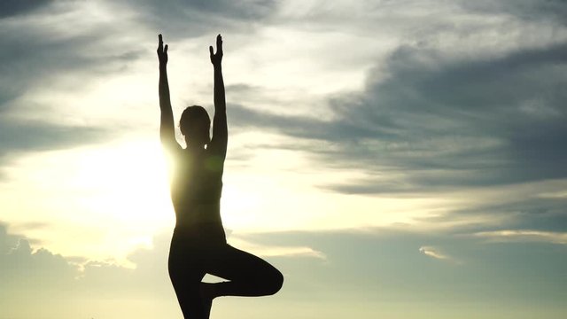 Silhouette young woman practicing yoga on the beach at sunset. 4K Resolution