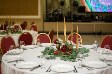 The wedding table setting is decorated with fresh flowers in a brass bowl and golden candles in brass candlesticks. Wedding floristry. Banquet table for guests. Bouquet with dahlias and eucalyptus