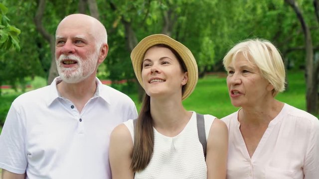 Happy family having great time enjoying summer vacation together. Senior couple with young teenage daughter walking in park laughing and chatting
