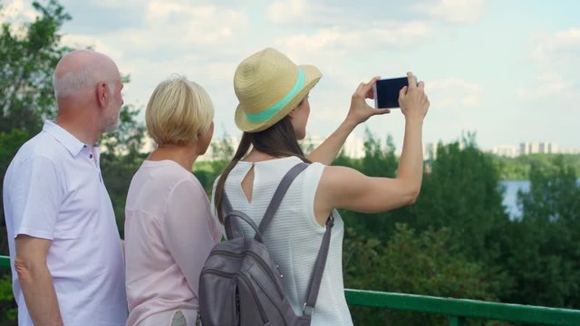 Happy family having great time enjoying summer vacation together. Senior couple with young teenage daughter in park looking from observation deck taking photo