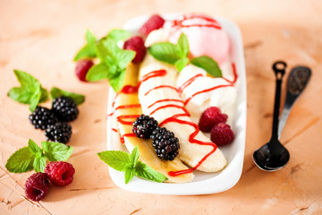 Summer fruit berry breakfast. Healthy banana split breakfast with white and pink ice cream , raspberries, blackberries, mint. On white plate. Selective focus