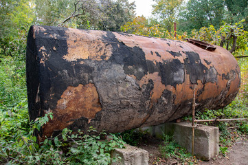 Old dilapidated water tank coated with stains of shabby black paint on rusty metal surface. Old vintage barrel on green outdoor place in Sofiyivsky park 