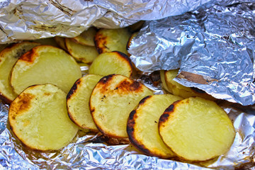 Fried potatoes in coals in aluminum foil close-up.