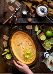Overhead shot of homemade casserole, pudding, cheesecake, tart, pie or mousse with slices of lime on top in oval glass baking dish on woman hand