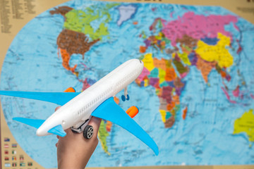 The hand of a man holds a plane with blue wings against the background of the atlas of the world. The concept of travel around the world.