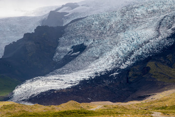 Tongue of Glacier Eyjafjallajökull in Iceland drifting down from the green moss mountain in the foggy day. Blue glacier ice is visible, as well as green moss covering rocks of the mountain