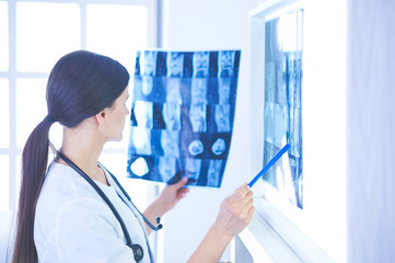 Young smiling female doctor with stethoscope pointing at X-ray at doctor's office