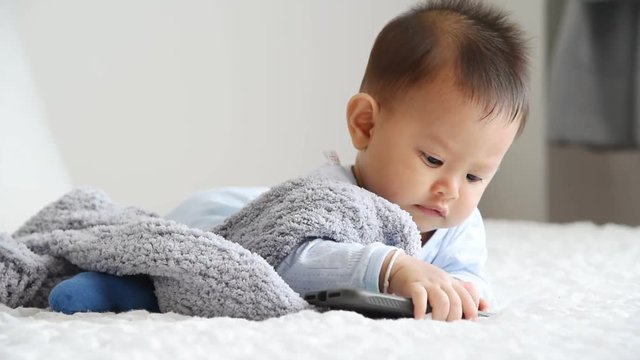 A little boy who is crawling, playing mobile phone in a white bed, smiling in a good mood, to baby concept.
