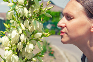 A beautiful and young girl, walking down the street, sniffs a beautiful Yucca flower and enjoys the aromatic smell of the plant.