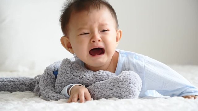 A little baby who is crawling, playing in a white bed, Are crying and demanding attention from the mother, to baby concept.