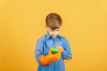 A boy in a blue shirt and orange gloves examines a green washing sponge.