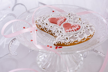 beautiful homemade gingerbreads as two herats  for a wedding celebration or Valentine's day on a glass cake stand  and white background next to bridal veil, closeup