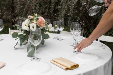 The waiter serves banquet table. Wedding table setting decorated with flowers and brass candlesticks with candles