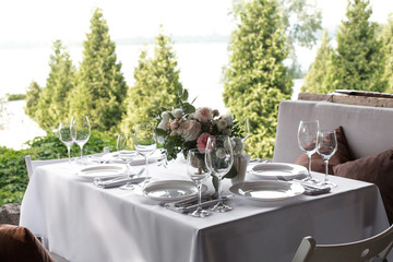 Wedding table setting decorated with fresh flowers in a brass vase. Wedding floristry. Banquet table for guests outdoors with a view of green nature. Bouquet with roses, eustoma and eucalyptus leaves