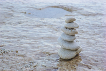 Fototapeta na wymiar Balance zen stones pyramid on pebble beach with a splashing wave. Stability, balance, and harmony concept