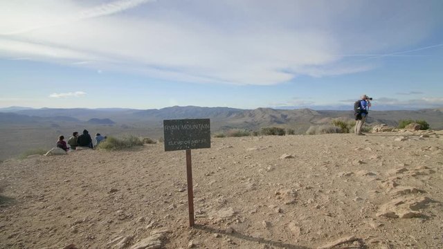 Scenic view atop Ryan Mountain with photographer and hikers enjoying the desert brown mountain blue sky view above.