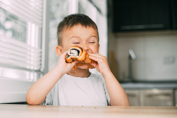 charming child in the kitchen during the day eating a bun with poppy seeds, very tasty