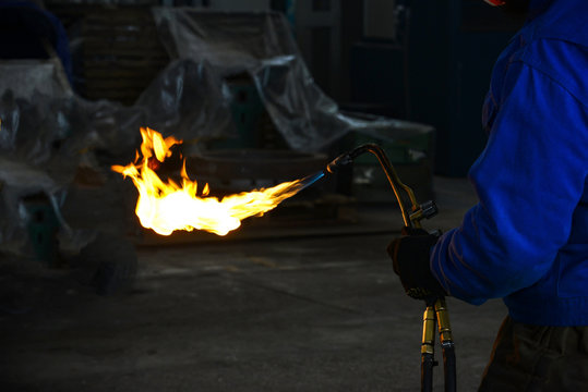 The welder holds the gas torch in his hand, the fire and the flame burns from the nozzle.