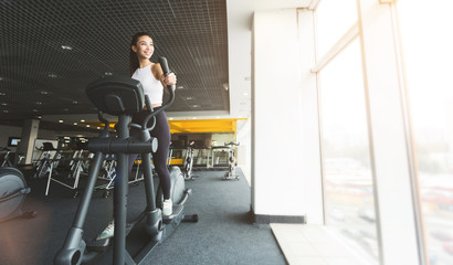 Fitness workout. Girl exercising on elliptical trainer in gym