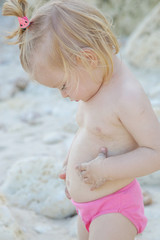 Candid portrait of a cute blonde baby girl enjoying a day at the rocky beach	