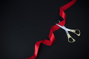 Grand opening. Top view of gold scissors cutting red ribbon on black background. - obrazy, fototapety, plakaty