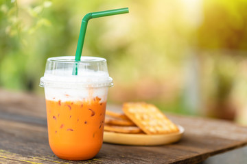 Iced Thai tea in clear plastic cup served on wooden table in garden cafe.
