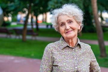 Portrait of an attractive fashionable elderly woman in the park. Pensive look with a sad smile....