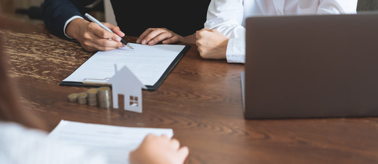 Couples signed a contract to buy a house from the broker. Coin to stack money and model house...