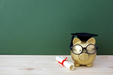 Gfold piggy bank with a grad cap and diploma in front of green chalkboard. Education scholarship