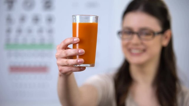 Woman in spectacles showing glass with carrot juice, beta carotene, vitamins