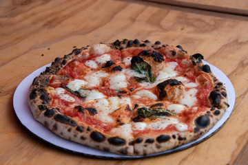 Round gourmet cheese pizza with red sauce and basil leaves with several burnt portions on a wooden tabletop