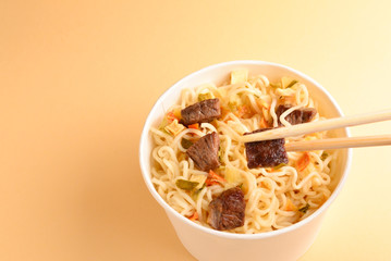 Paper cup with instant ramen noodles with beef and vegetables.