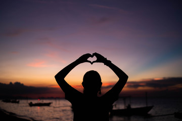 Woman making heart symbol with hands at sunset.