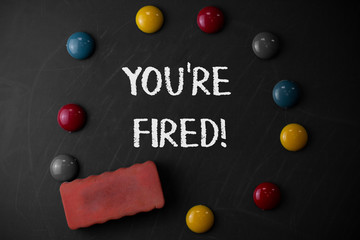 Word writing text You Re Fired. Business photo showcasing Used by boss indicate employee that he is discharged from job Round Flat shape stones with one eraser stick to old chalk black board