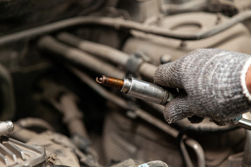 A serviceman repairs a car while replacing the spark plugs while holding one of them in hand with a...