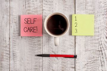 Writing note showing Self Care. Business concept for practice of taking action preserve or improve ones own health Stationary placed next to a cup of black coffee above the wooden table