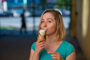 Portrait of a cute girl in a green dress is walking outside and eating dessert. Beautiful blonde enjoying a cone with ice cream on a beautiful summer day. Life is a pleasure