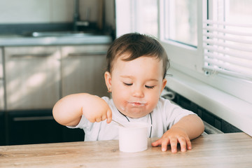 A little charming girl eats yogurt all smeared herself