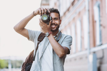 Young man photographer takes photographs with dslr camera in a city. Travel, vacations, professional freelance work and active lifestyle concept