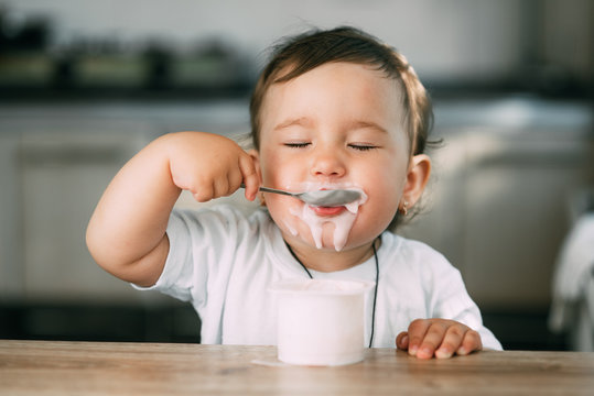 A little charming girl eats yogurt all smeared herself