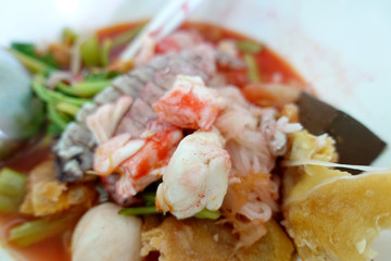 Yentafo Spicy noodle soup,hot and spicy ,with mix seafood, crayfish, shrimp. Asian spicy seafood noodle soup in white bowl on table background. Thai style noodle and street food of Thailand.