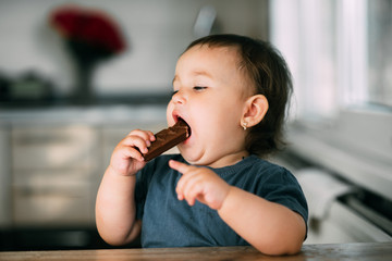 little girl in the afternoon in the kitchen eating a delicious chocolate bar