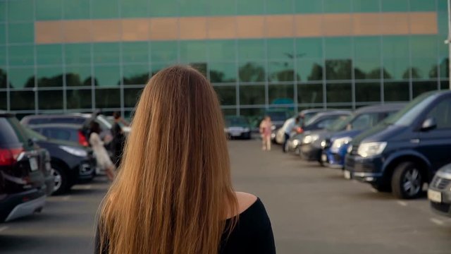 The camera follows a young attractive brunette in the parking lot.