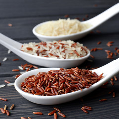 Different types of rice in spoons on wooden table background