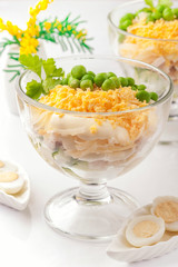 Chicken salad with mayonnaise. With a side dish of cucumber, green peas and boiled egg yolk. Served portion in glassware. Close up and vertical view.